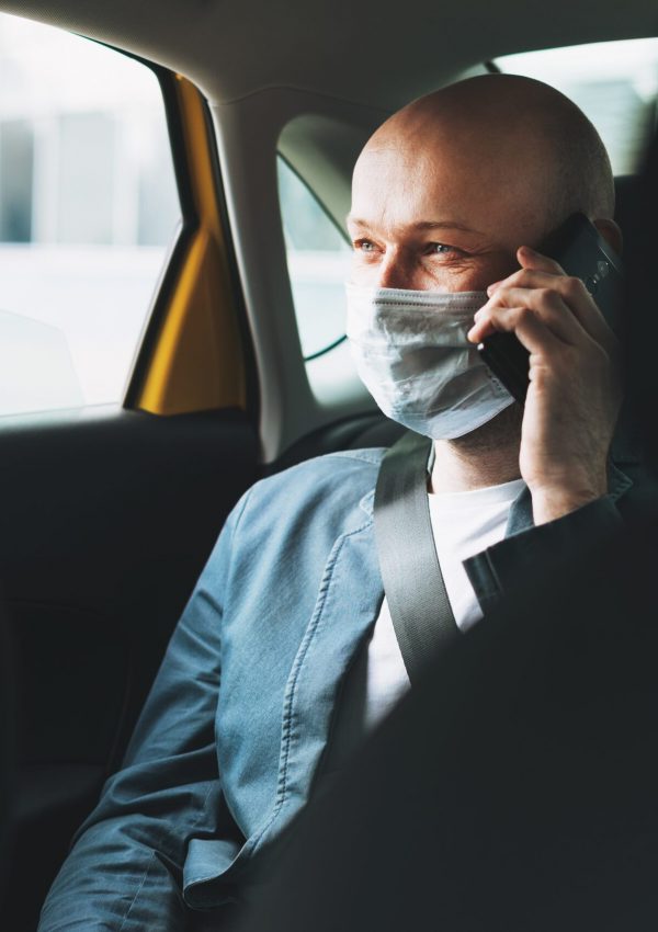 Bald man businessman in medical face mask using mobile phone inside yellow car taxi. Concept of coronavirus quarantine